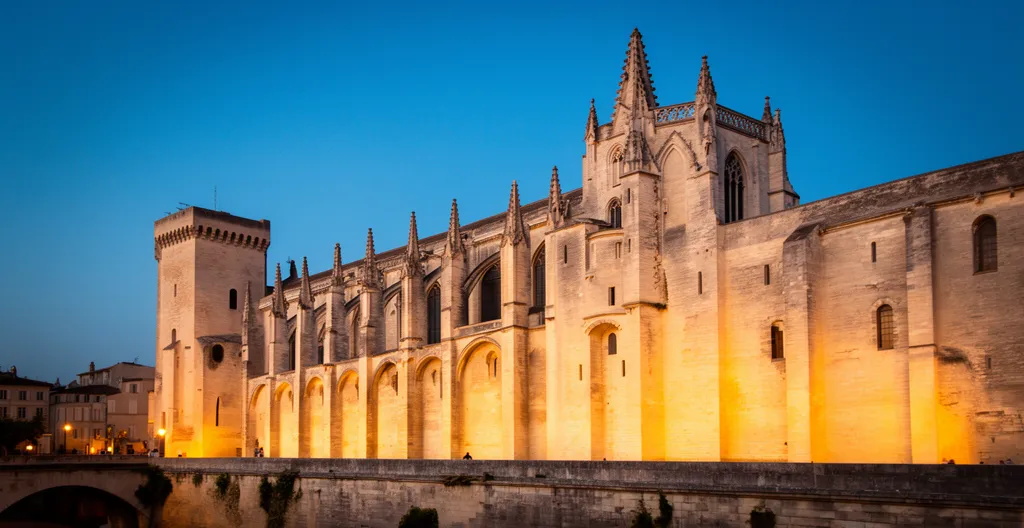 Vue atmosphérique de la Cité des Papes d'Avignon au crépuscule, mêlant architecture gothique et lumières dorées
